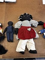 Two black rag dolls, one in red polka-dot dress and white pants, the other smaller in dark overalls, lying on brown surface.