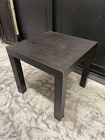Angle view of the small square table showing dark brown color and worn surface with scratches.