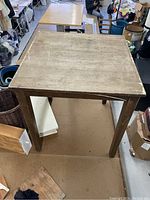 Square wooden table showing the top surface and legs, with visible wear and weathering on the tabletop and edges.