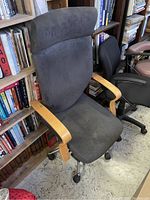 Front view of black fabric upholstered swivel office chair with wooden armrests and headrest cushion.