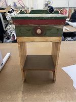 Front view of vintage wooden cupboard showing the worn paint and overall structure with drawer closed and lower shelf.