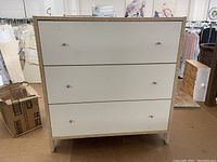 Front view of white cupboard cabinet showing three drawers with silver round knobs.