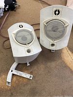 Pair of white Solid speakers with wiring and two stands, one stand broken showing repairable damage.