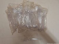 Multiple clear plastic forks sealed in plastic packaging along with one fork removed and placed in front for display.