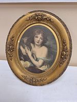 Full view of the antique framed oval artwork showing the girl and lamb portrait and ornate gold frame.