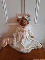 Front view of Bearington plush bear in detailed white coat with fur trim and gold belt, sitting on wooden surface.