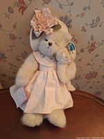 Cream-colored Bearington Bears plush teddy bear dressed in a pink wafer knit dress with a large pink flower on head, holding a small teddy bear. Tags are attached.