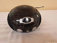 Front and top view of the black oval-shaped General Electric portable CD player with AM/FM radio. Shows control buttons, display screen, and speaker design.