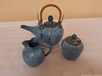 Blue pottery tea set displayed with the teapot, sugar jar, and creamer on a white surface.