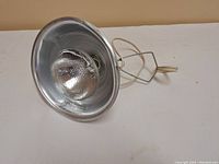 Full view of the clamp-on work light with reflector, showing the bulb inside the metal shade and clamp attached.