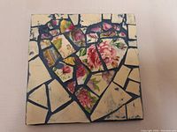 Square mosaic artwork showing the floral heart design with broken patterned crockery pieces on beige background