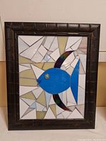 Full view of the framed mosaic tile art featuring a blue fish against a geometric tile background, dark brown textured frame.