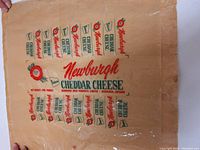 Full view of large square cream-colored wax paper cheese wrapper with red and green Newburgh Cheddar Cheese branding and logos.
