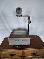 Front view of the vintage overhead projector showing the glass surface, lens, and projection arm.