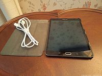 Samsung Galaxy Tab 52 tablet in black with Fintie cover and white charging cable on wooden table.