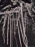 Six silver chains of varying thicknesses and lengths displayed laid flat on black velvet fabric surface.