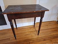 Full view of vintage wooden table showing rectangular top and four turned legs. Table finish is worn, with edge wear visible.