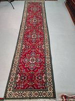 Full-length view of the runner rug showing red field with repeating geometric medallions, beige border and cream fringe.