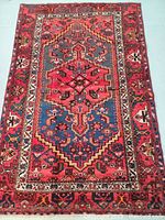 Full view of hand knotted Persian wool rug with geometric central medallion and intricate border in red and cobalt blue colors.