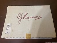 Closed cardboard box with 'A.J. Casson' written on top, label showing lot number 103.