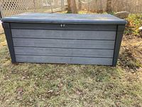 Front view of weathered outdoor plastic storage box with hinged lid showing horizontal panel design and latch on the front.