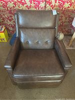 Front view of the brown faux leather recliner chair showing button tufted backrest and seat cushion, padded armrests.