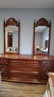 Front view of the Peppler wood dresser with two attached tall mirrors, showing wooden carved details and brass handles.