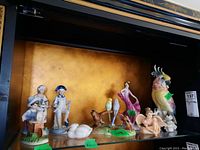 Full view of all figurines displayed on a shelf, showing various animal and human figures including a large parrot and children.
