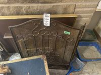 Metal fireplace screen leaning against wall with decorative wrought iron scroll design and mesh center