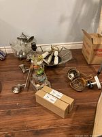 Various ceiling light fixtures with metal and glass parts and electrical components including bulbs and chains on wooden floor next to a box.