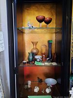 Full view inside cabinet showing multiple decorative glassware, miniature animal figurines, and vases.
