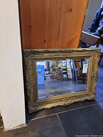Front view of rectangular mirror with ornate plaster frame leaning against wall.