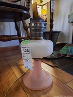 Side view of the vintage glass oil lamp showing pink base, white hobnail reservoir, and metal burner assembly with tag 'oil lamp'.
