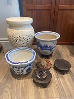 Frontal view of white carved ceramic pedestal, two blue and white planters, and four wooden pedestal stands
