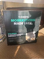 Box front with Dometic branding and mobile living slogan, showing 5 gallon capacity portable toilet image.
