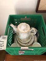 Royal Albert bone china tea set inside green milk crate, showing teapot with lid and plates/saucers stacked under it.
