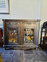 Front view showing two glass paneled doors with leaded lattice design and two drawers above featuring carved floral designs.