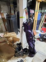 Full view of the skis, ski boots, helmet, and purple ski bag in a basement setting.