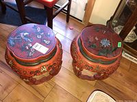 Two lacquered Chinese stools side by side on wooden floor showing details of paint and wear.