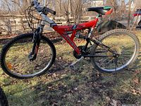 Side view of the red and black Supercycle CTI-21DS mountain bike outdoors on grass with leaf litter. Shows frame, wheels, and saddle clearly.