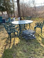 Full view of metal round table with glass top surrounded by 4 green metal chairs and 6 large cushions stacked in front.