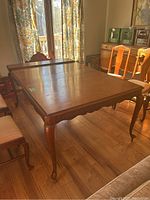 Vintage wooden dining table on casters shown with one leaf installed, placed in a room with wooden floor and natural light.