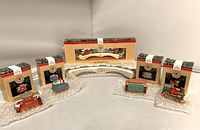 Full set of Hallmark Claus & Co. miniature train ornaments with the display bridge arranged on a soft padding surface with light gray background.
