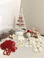 Holiday decorations including white Christmas tree-shaped ornaments with red bows, red bead garland, decorative snowflakes, Santa and animal figurines, and pink/white baubles.