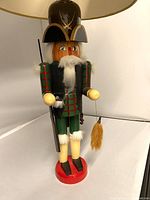 Front angled view of the Hunter Nutcracker lamp showing the painted wooden figure, detailed outfit, and large hat with lamp shade on top.