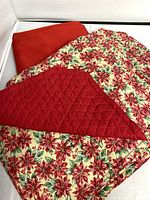 Photo showing folded large red rectangular tablecloth alongside six poinsettia print reversible placemats.