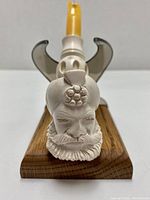 Front close-up view of carved meerschaum pipe head shaped like a bearded man with detailed face and headwear, on Mudi display stand.