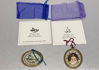 Two White House ornaments, each with their brochures and protective sheer bags in blue and purple, showing front views of both ornaments.