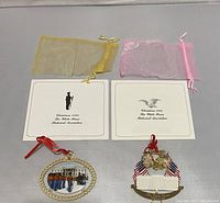 Two White House Christmas ornaments with their multipage brochures and organza storage bags, laid flat on surface.