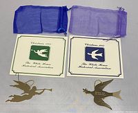 Three brass-colored metal White House Historical Association Christmas ornaments with their brochures and mesh bags. Two brochures marked Christmas 1981 and Christmas 1982 included.
